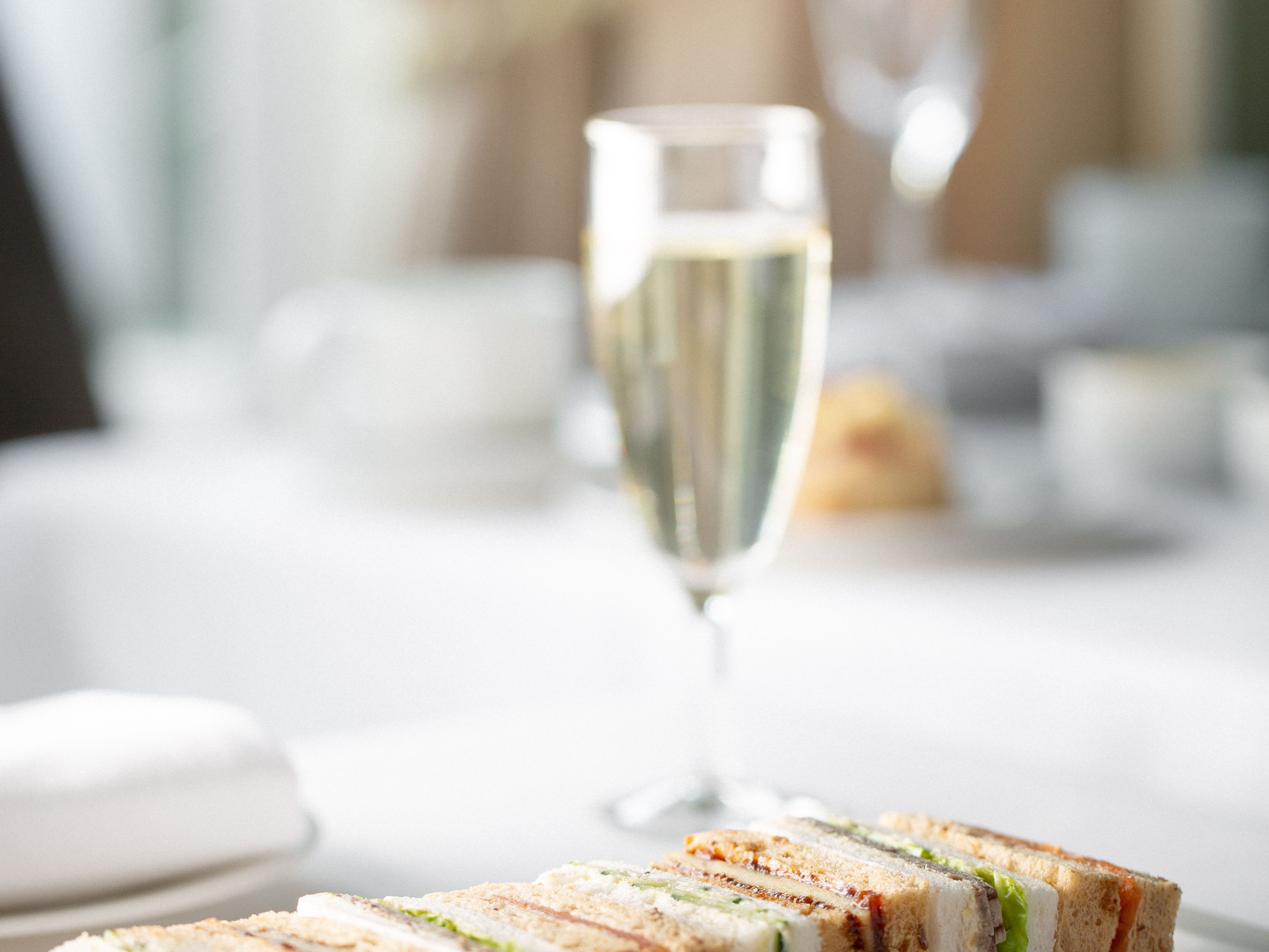 A plate of assorted finger sandwiches next to a glass of sparkling wine on a white tablecloth.