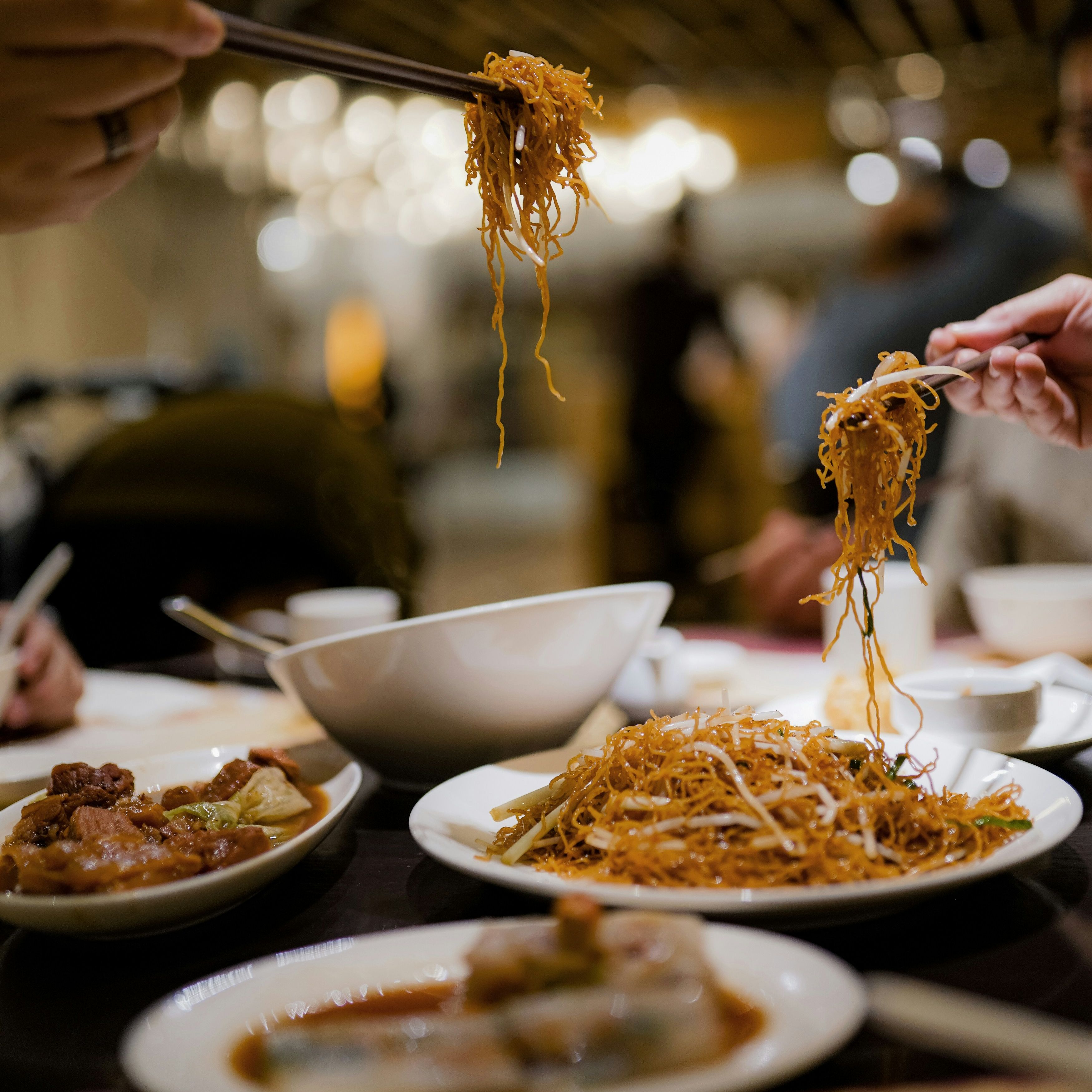 People sharing and eating noodles with chopsticks at a restaurant table