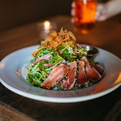 Plate of seared tuna salad with greens and crispy wontons on a wooden table