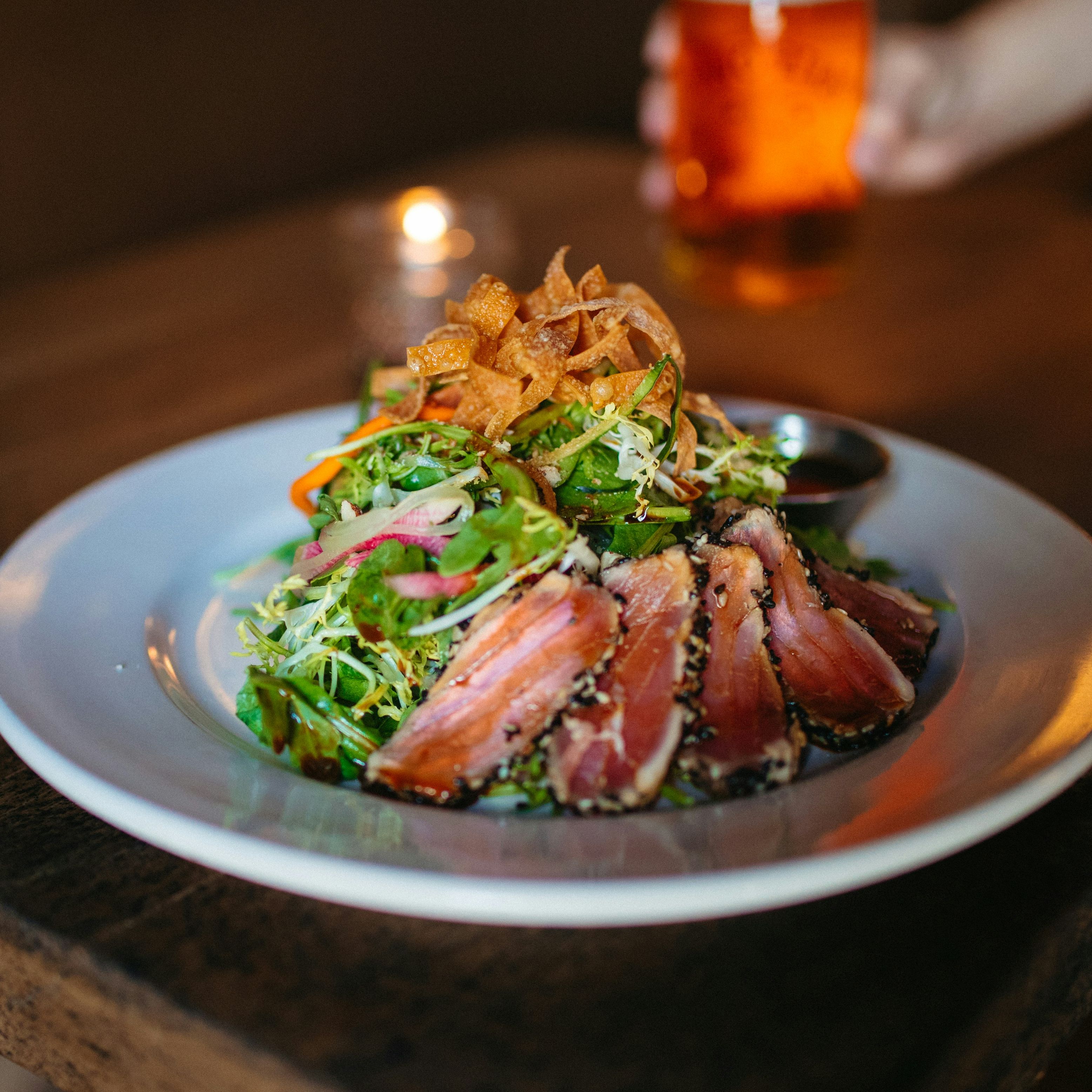Plate of seared tuna salad with greens and crispy wontons on a wooden table