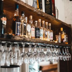 Assorted liquor bottles and wine glasses hanging upside down on a wooden bar shelf