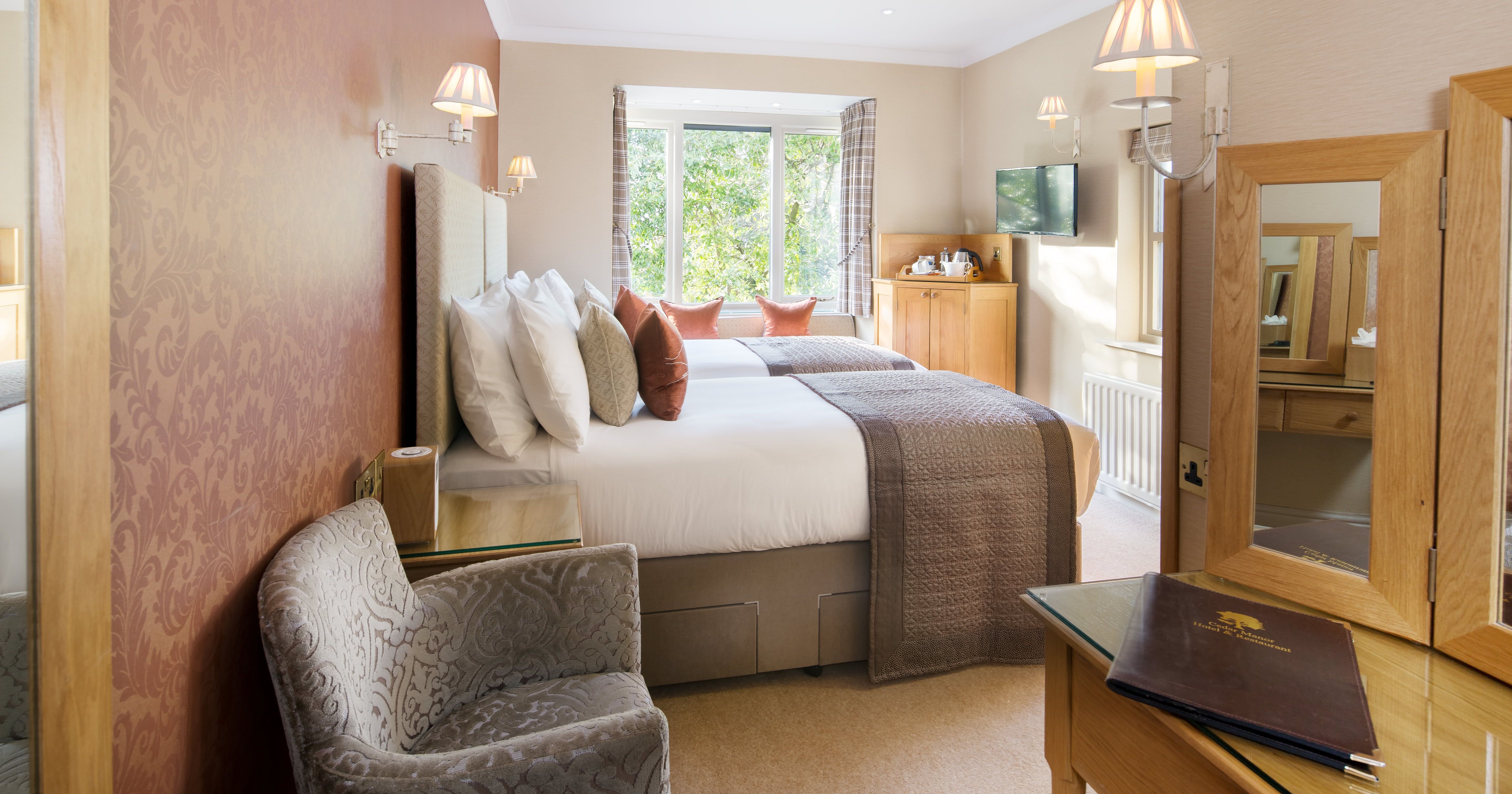 Elegant twin hotel room with two beds, a window seat, and wooden furniture.