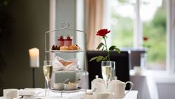Elegant afternoon tea set with pastries, scones, tea, and a single red rose on a white tablecloth