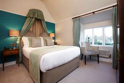 Elegant bedroom with a double bed, teal and beige decor, bedside lamps, armchair, and a large window with blue curtains.