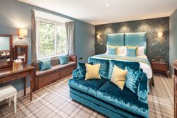 Elegant hotel room with blue and yellow accents, a large bed, sofa, vanity, and window seat.