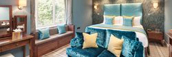 Elegant hotel room with blue and yellow accents, a large bed, sofa, vanity, and window seat.