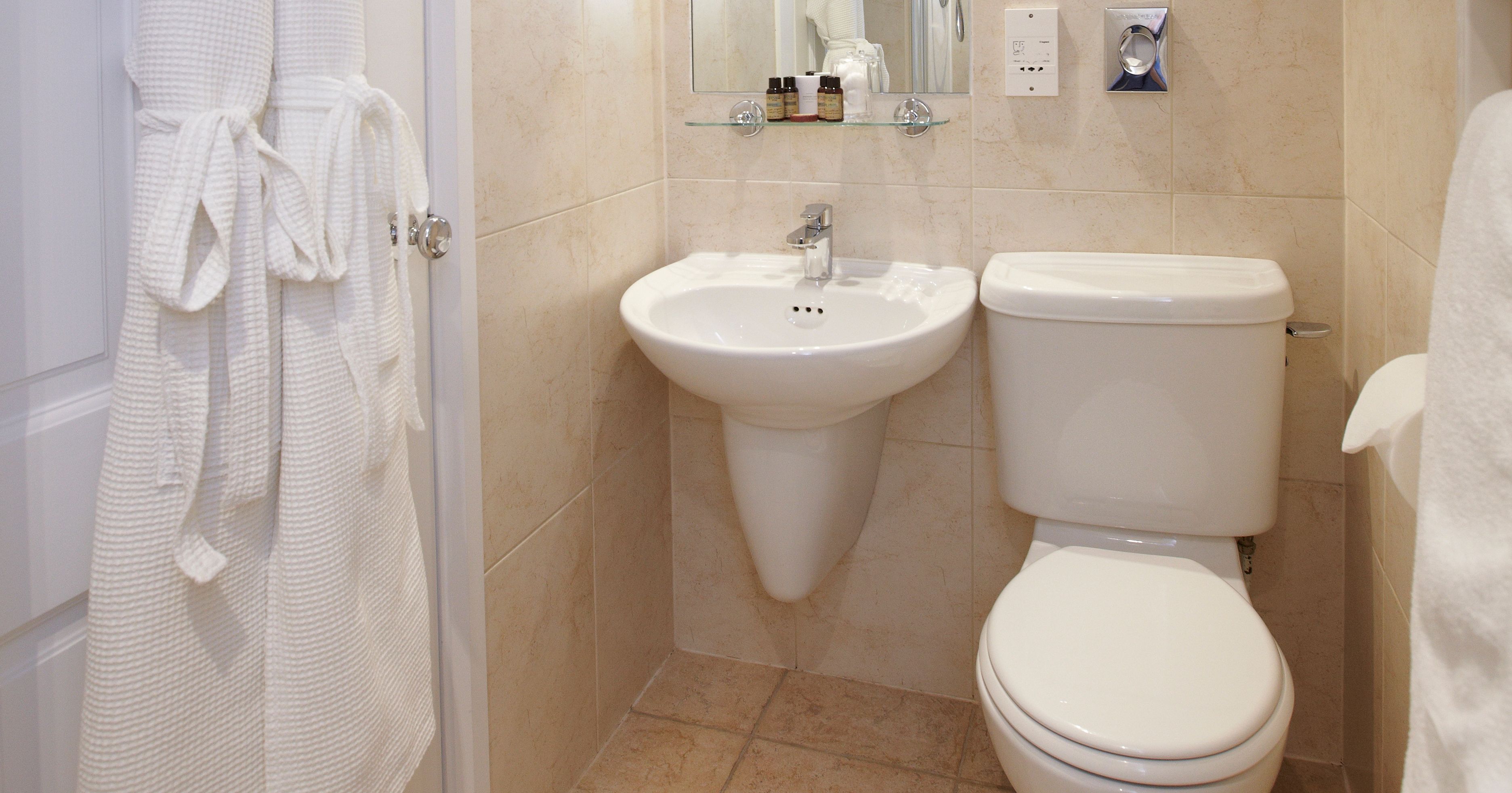 Modern ensuite bathroom with white sink, toilet, mirror, and bathrobe hanging on the door