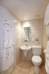 Modern ensuite bathroom with white sink, toilet, mirror, and bathrobe hanging on the door