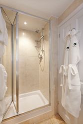 Modern tiled shower cubicle with glass doors and a bathrobe hanging on a hook