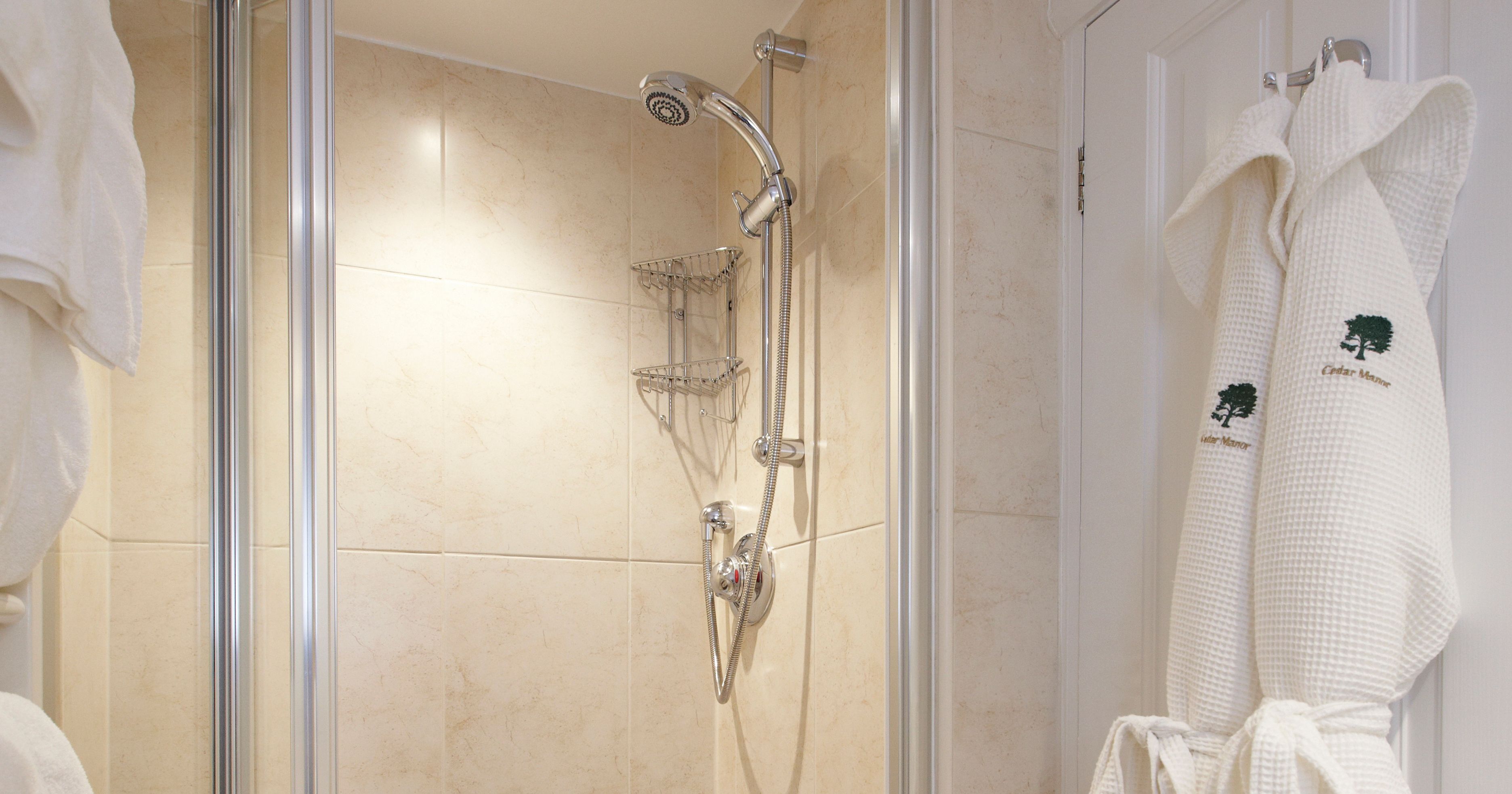 Modern tiled shower cubicle with glass doors and a bathrobe hanging on a hook