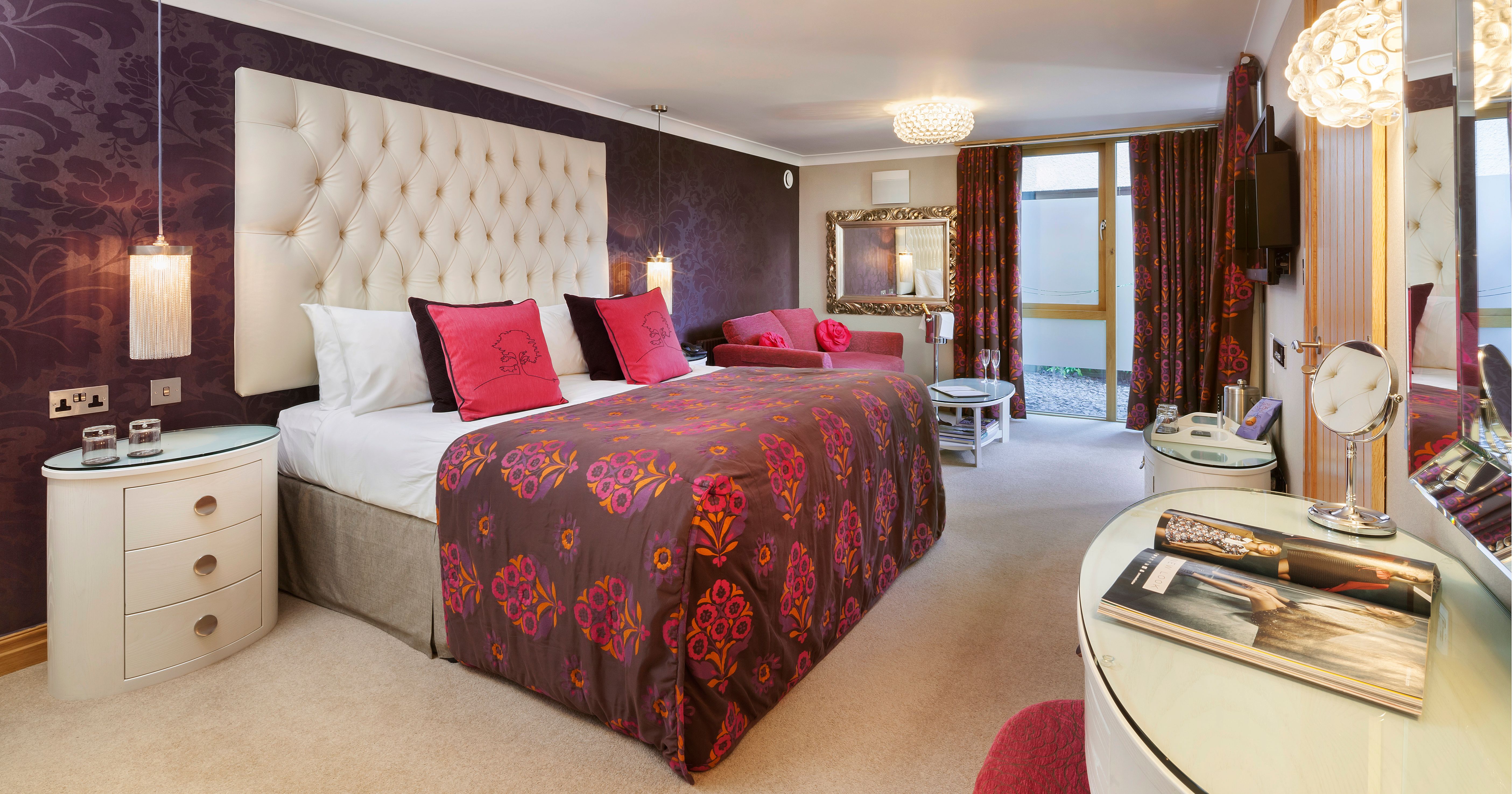 Elegant hotel bedroom with patterned bedspread, purple feature wall, and modern furnishings