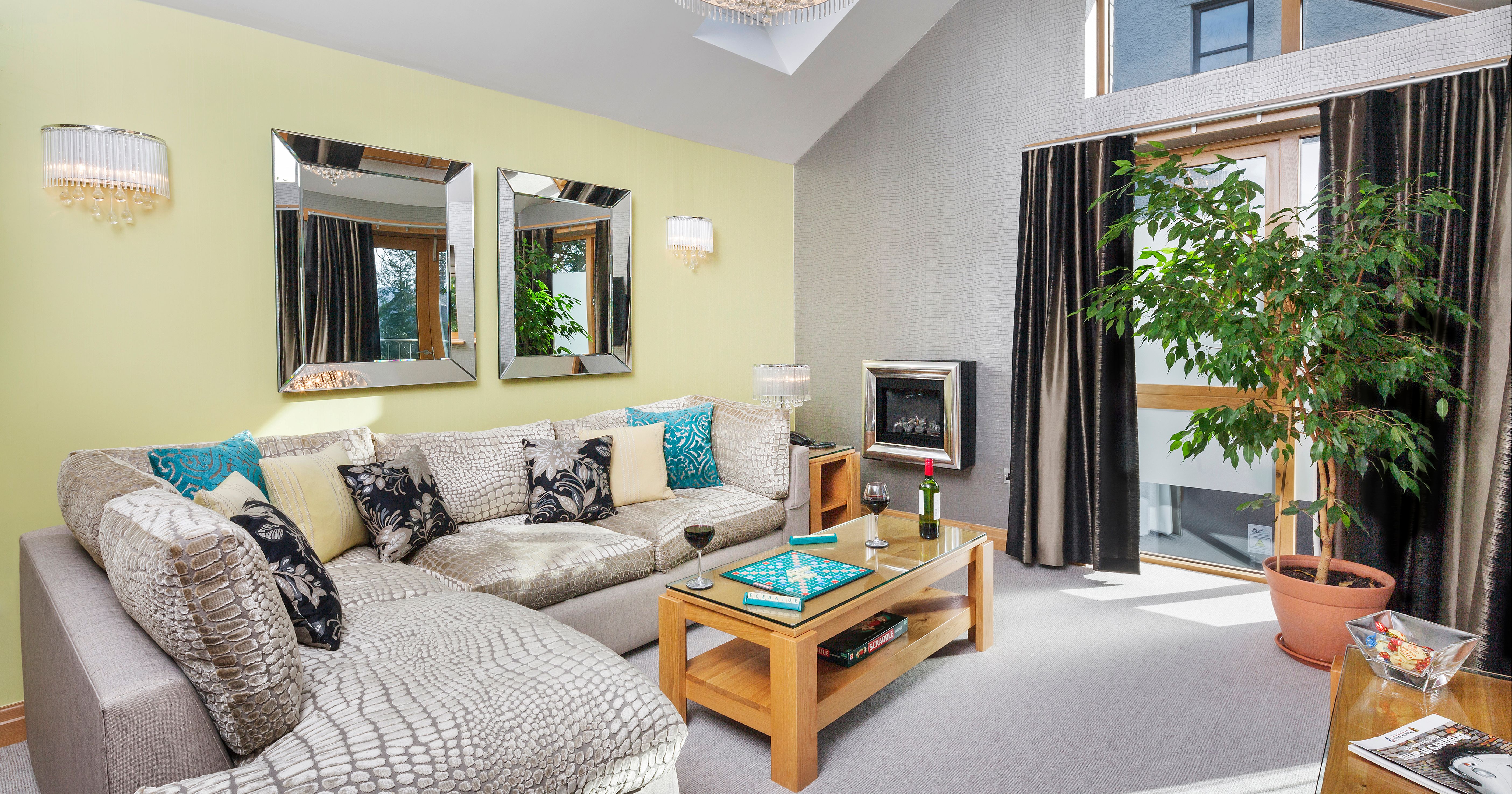 Modern lounge with sectional sofa, coffee table, fireplace, and large potted plant near window.