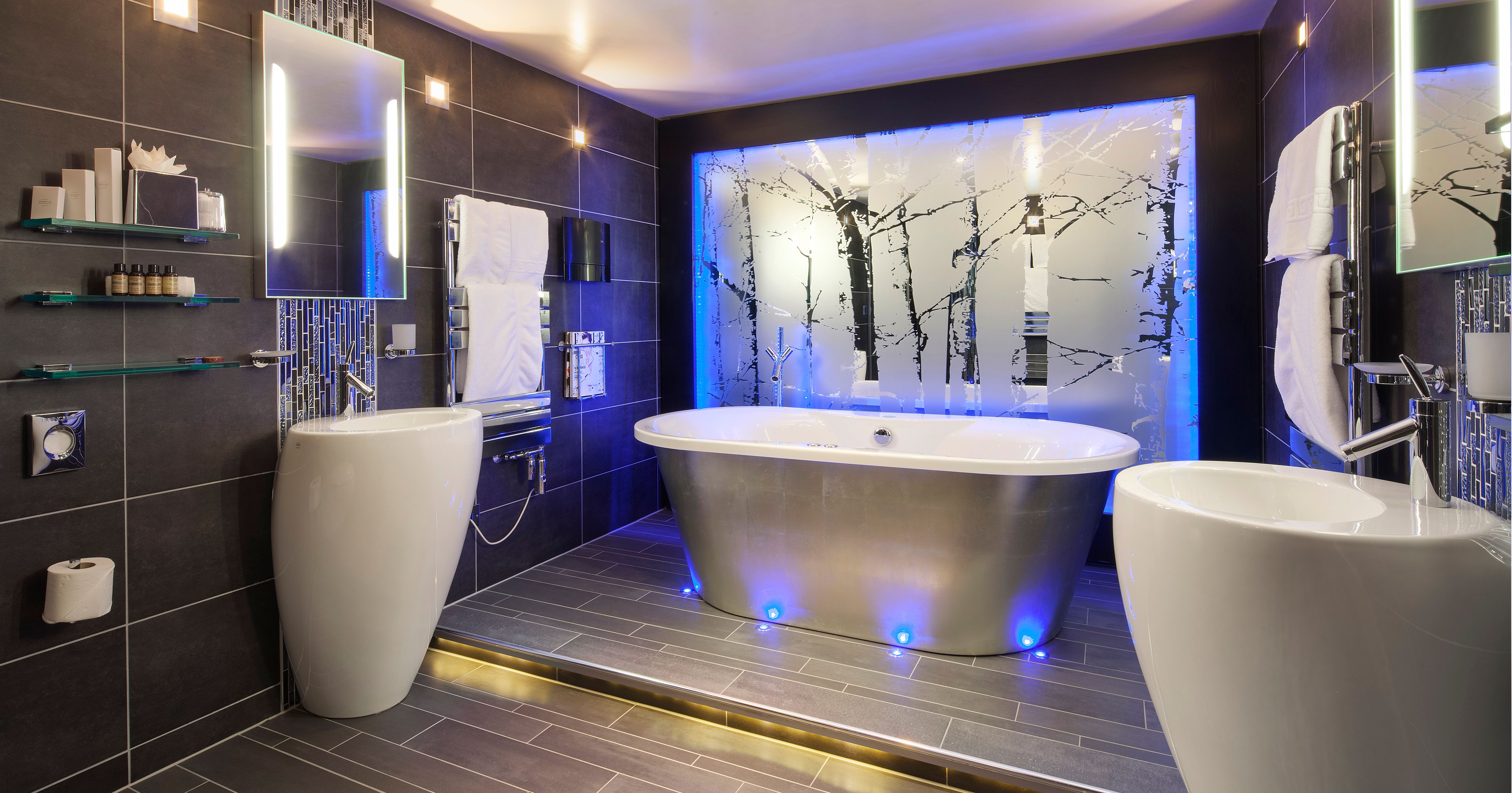 Modern ensuite bathroom with freestanding bathtub, illuminated blue lights, and frosted glass wall with tree design