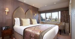 Elegant hotel room with large double bed, decorative headboard, and window seating area
