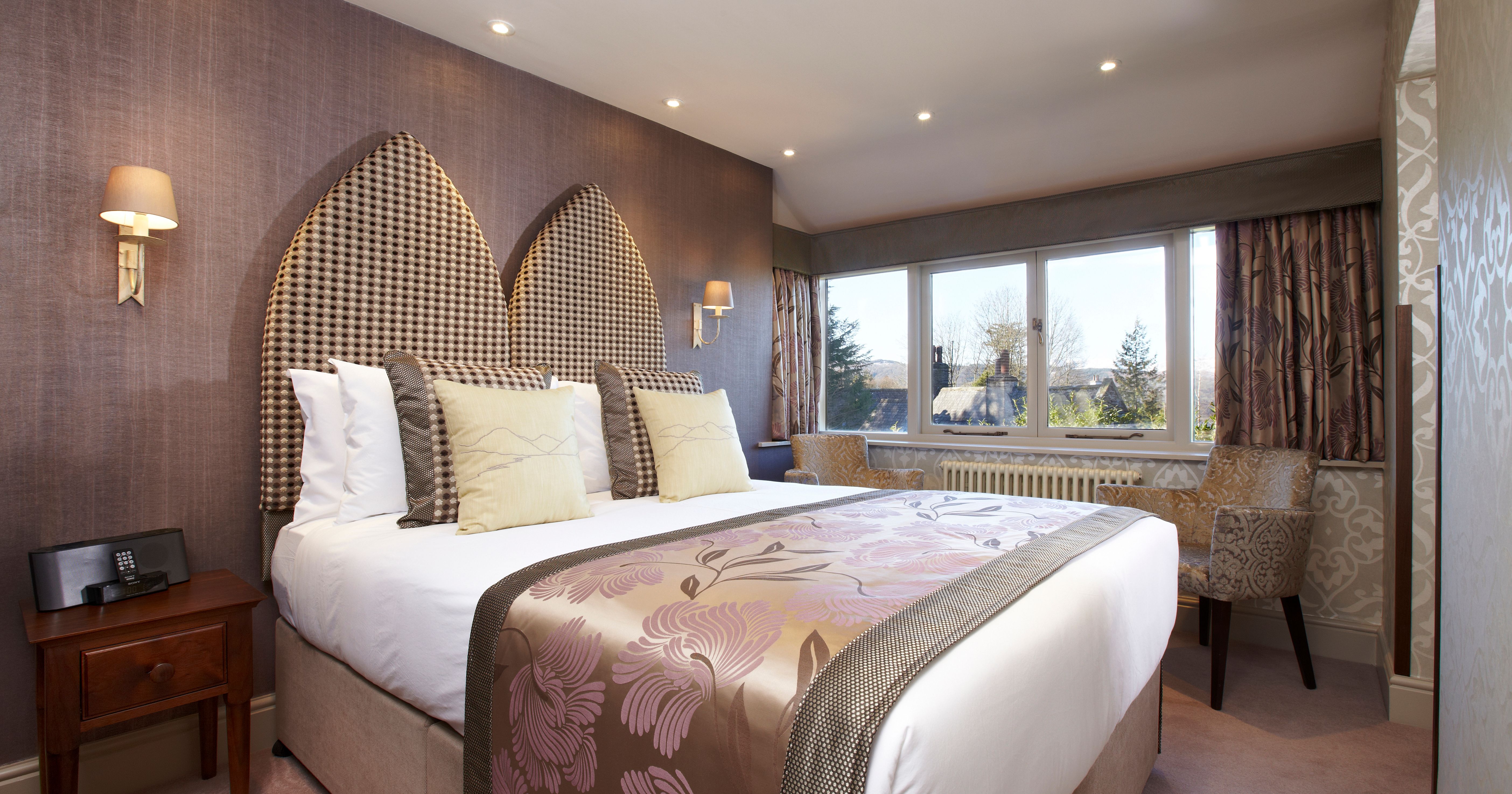 Elegant hotel room with large double bed, decorative headboard, and window seating area