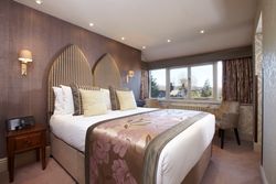 Elegant hotel room with large double bed, decorative headboard, and window seating area