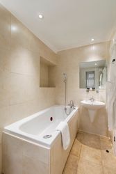 Modern bathroom with beige tiles, a bathtub, a sink, and a wall mirror.
