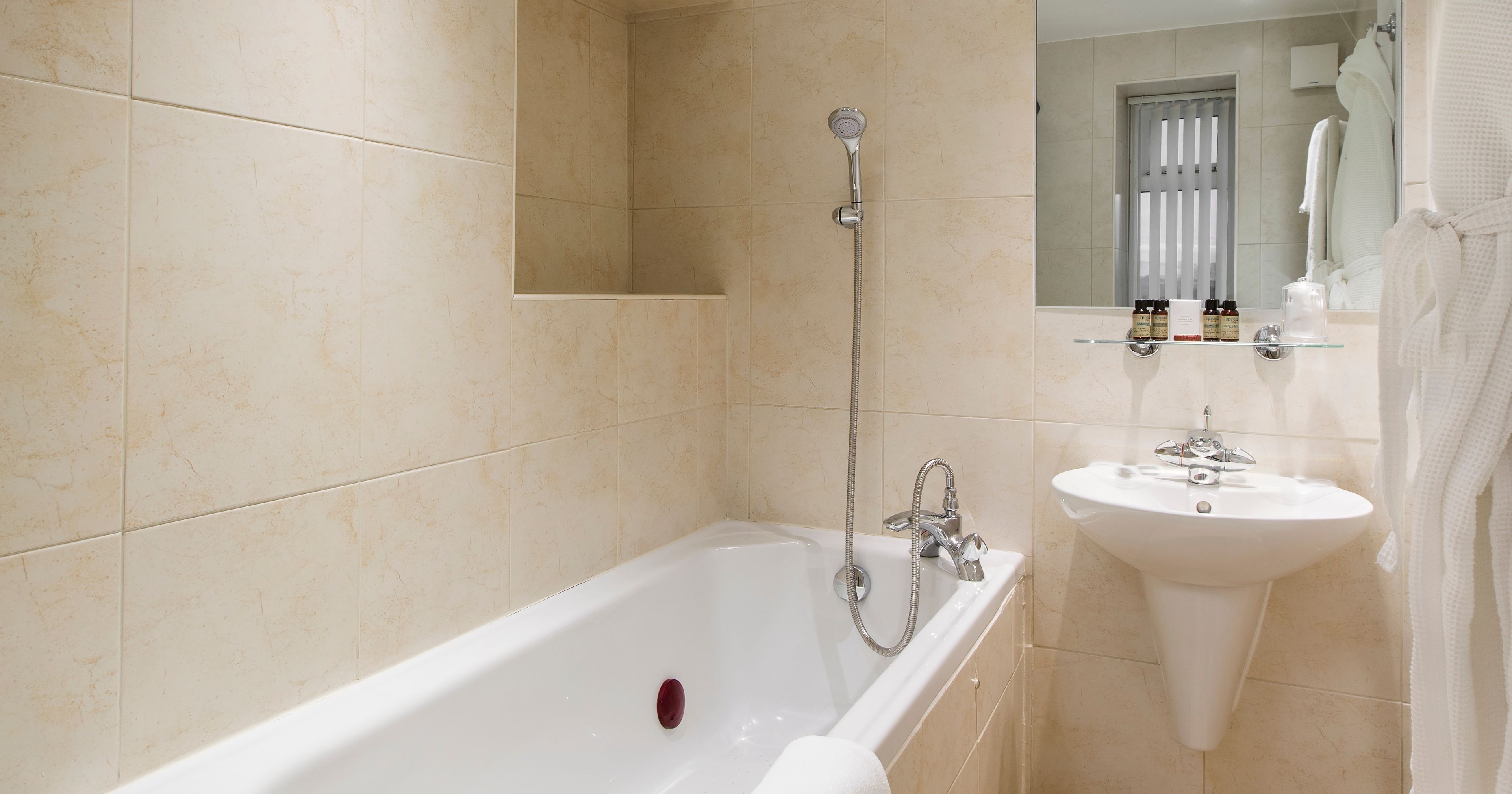 Modern bathroom with beige tiles, a bathtub, a sink, and a wall mirror.