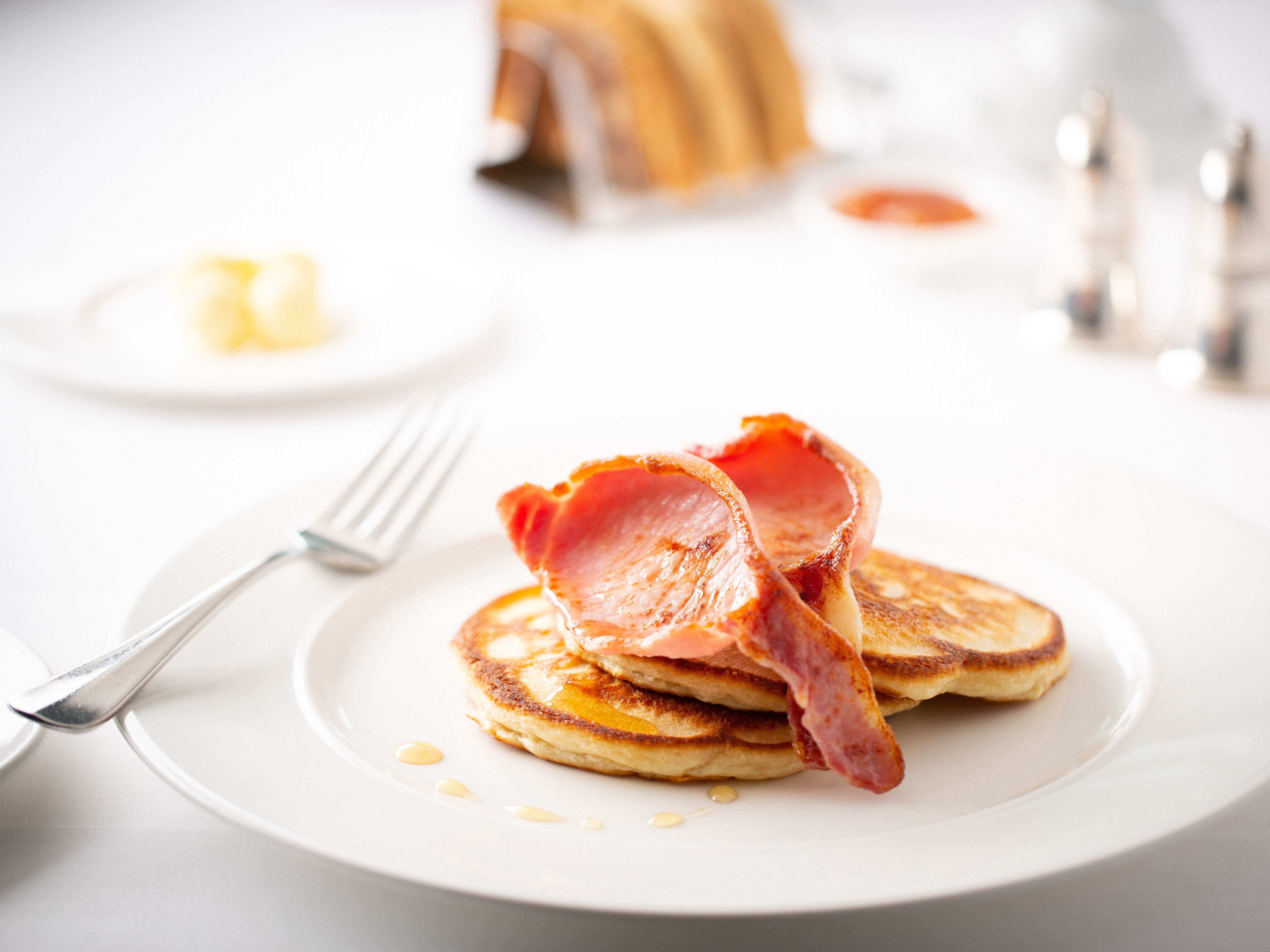 Plate of fluffy pancakes topped with crispy bacon on a white table setting