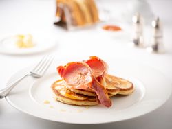 Plate of fluffy pancakes topped with crispy bacon on a white table setting