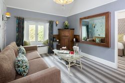 Modern lounge area with beige sofa, large mirror, and window seat in a hotel suite.