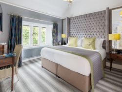 A modern, well-lit hotel room with a king-sized bed, decorative headboard, desk, and large window.