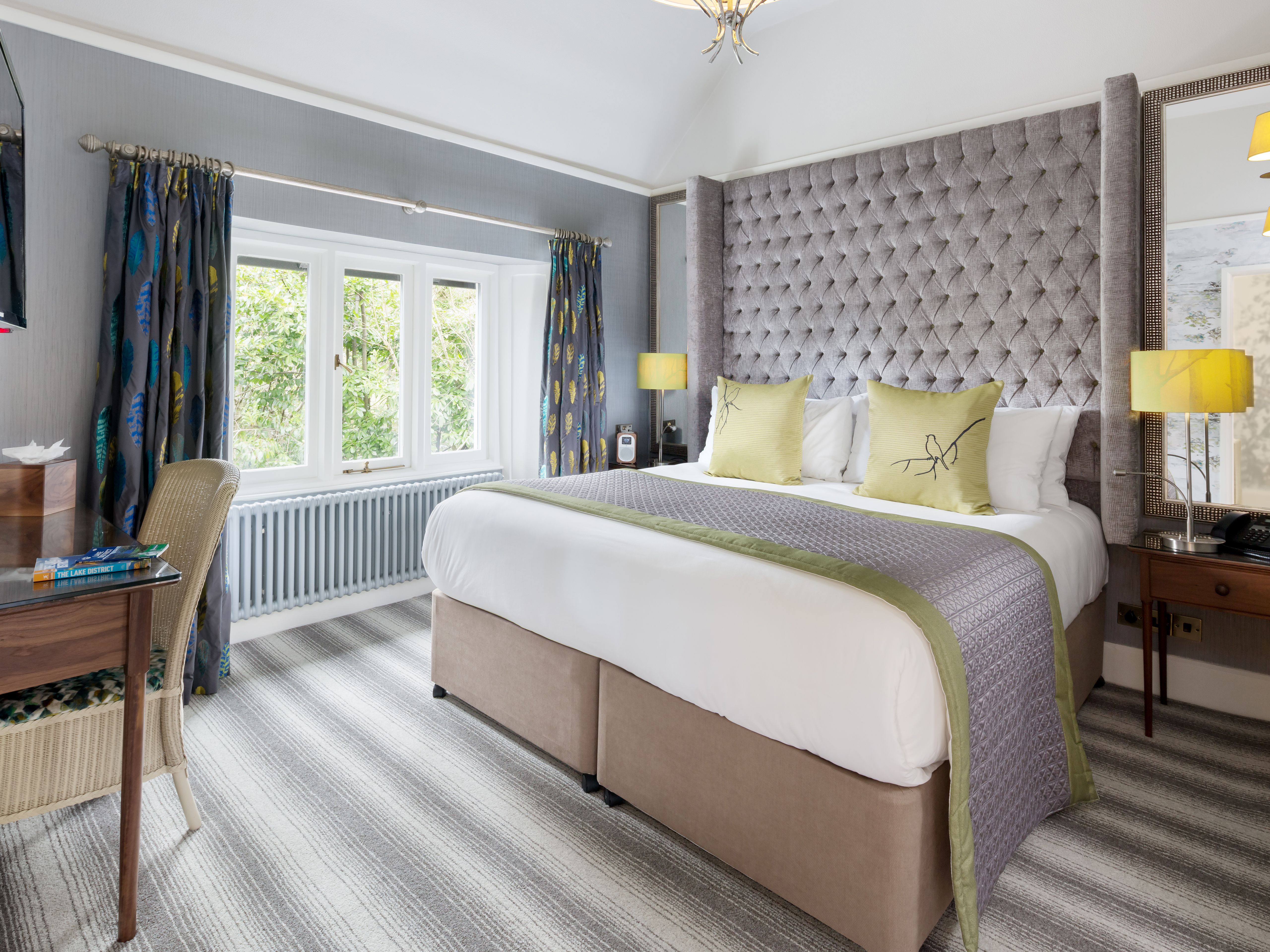A modern, well-lit hotel room with a king-sized bed, decorative headboard, desk, and large window.