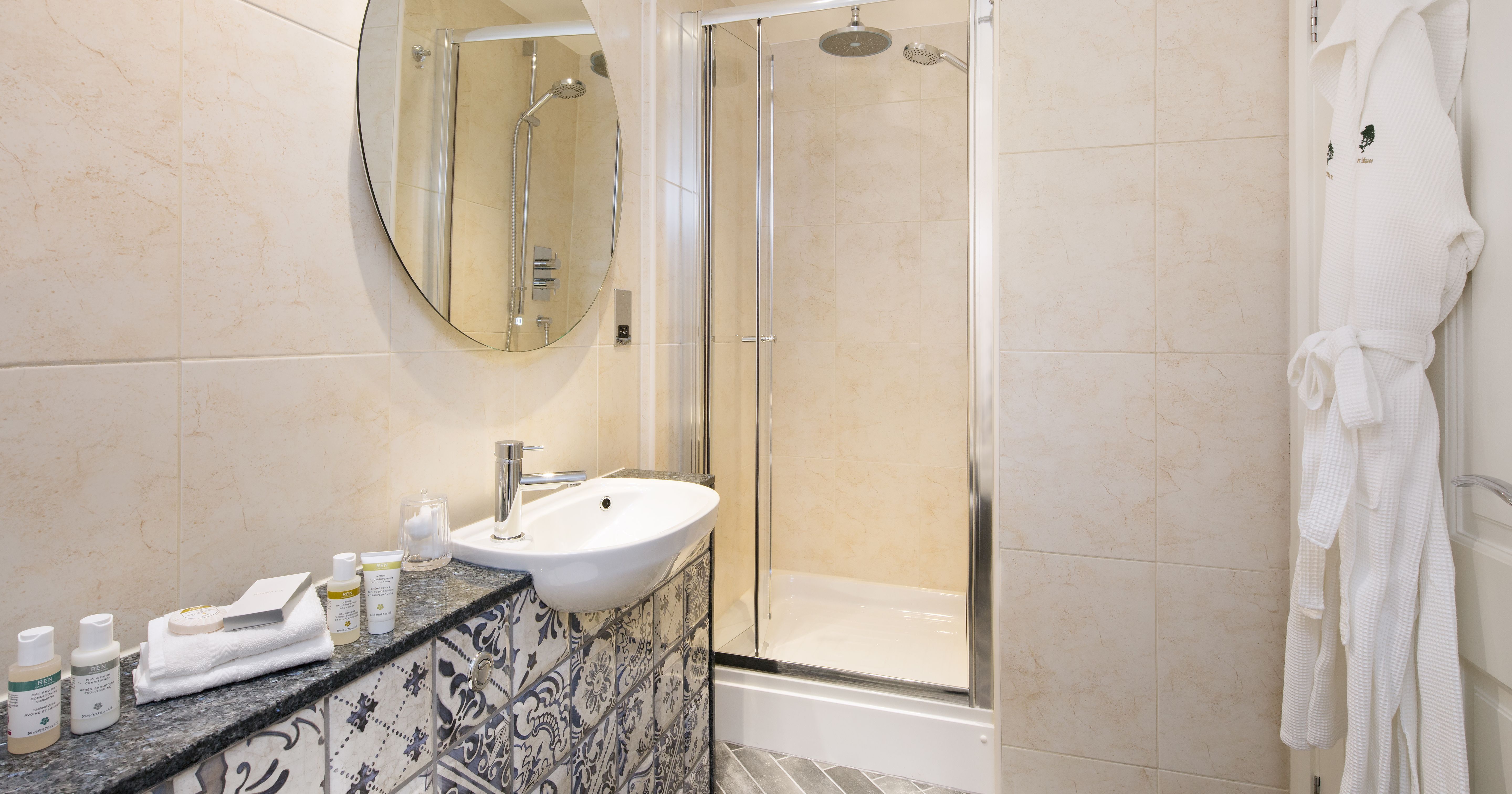 Modern en-suite bathroom with walk-in shower, patterned vanity, round mirror, and bathrobe