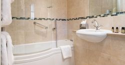 Modern bathroom with beige tiles, a bathtub with shower, towels, and a sink with toiletries.