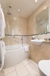 Modern bathroom with beige tiles, a bathtub with shower, towels, and a sink with toiletries.