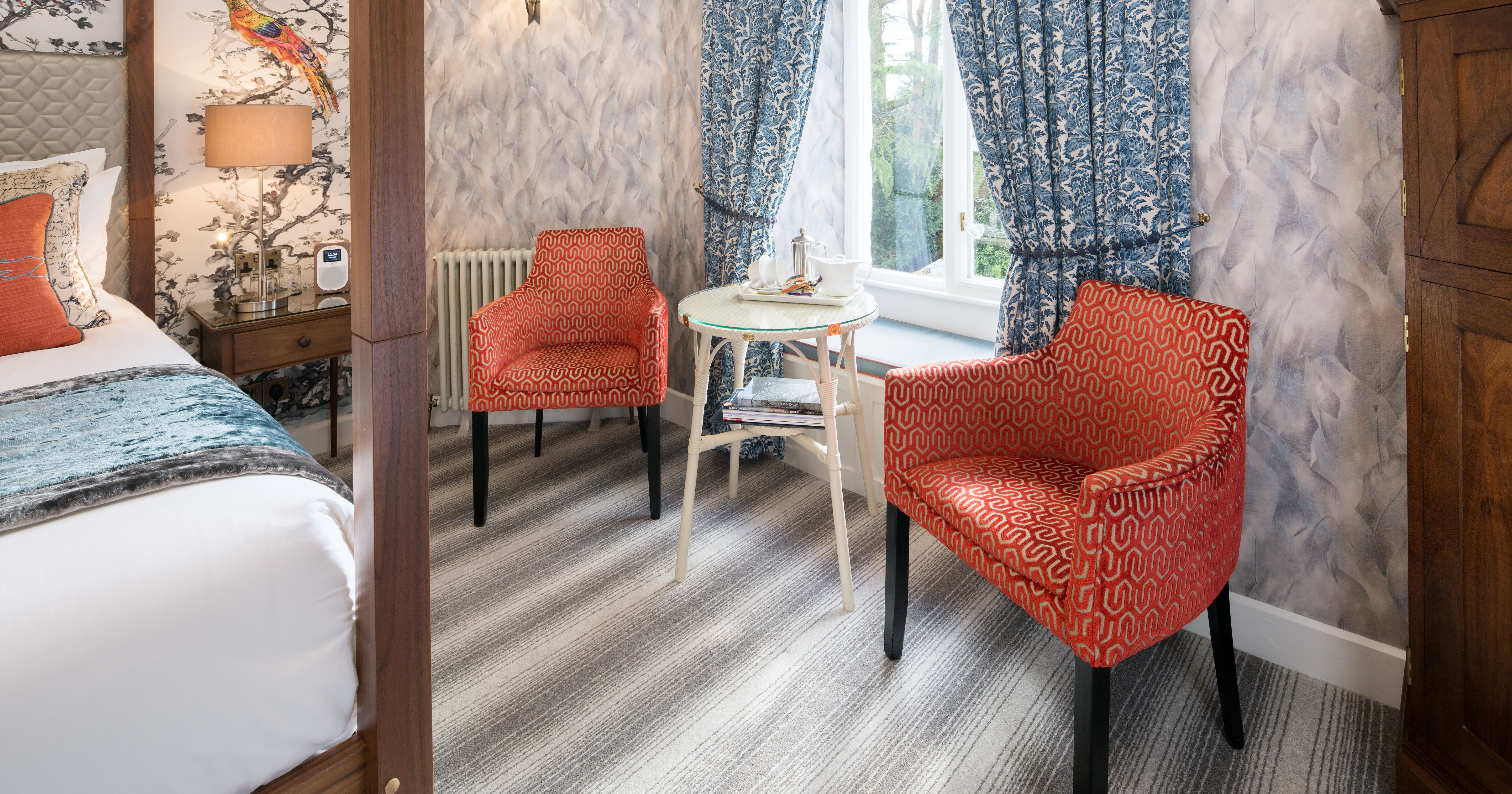 Cozy bedroom seating area with two orange patterned chairs, a small round table, and blue curtains by a window