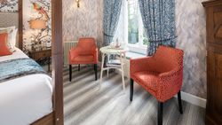 Cozy bedroom seating area with two orange patterned chairs, a small round table, and blue curtains by a window
