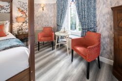Cozy bedroom seating area with two orange patterned chairs, a small round table, and blue curtains by a window
