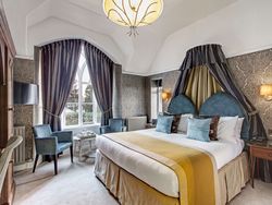 Elegant hotel bedroom with large bed, ornate curtains, and stylish seating area.