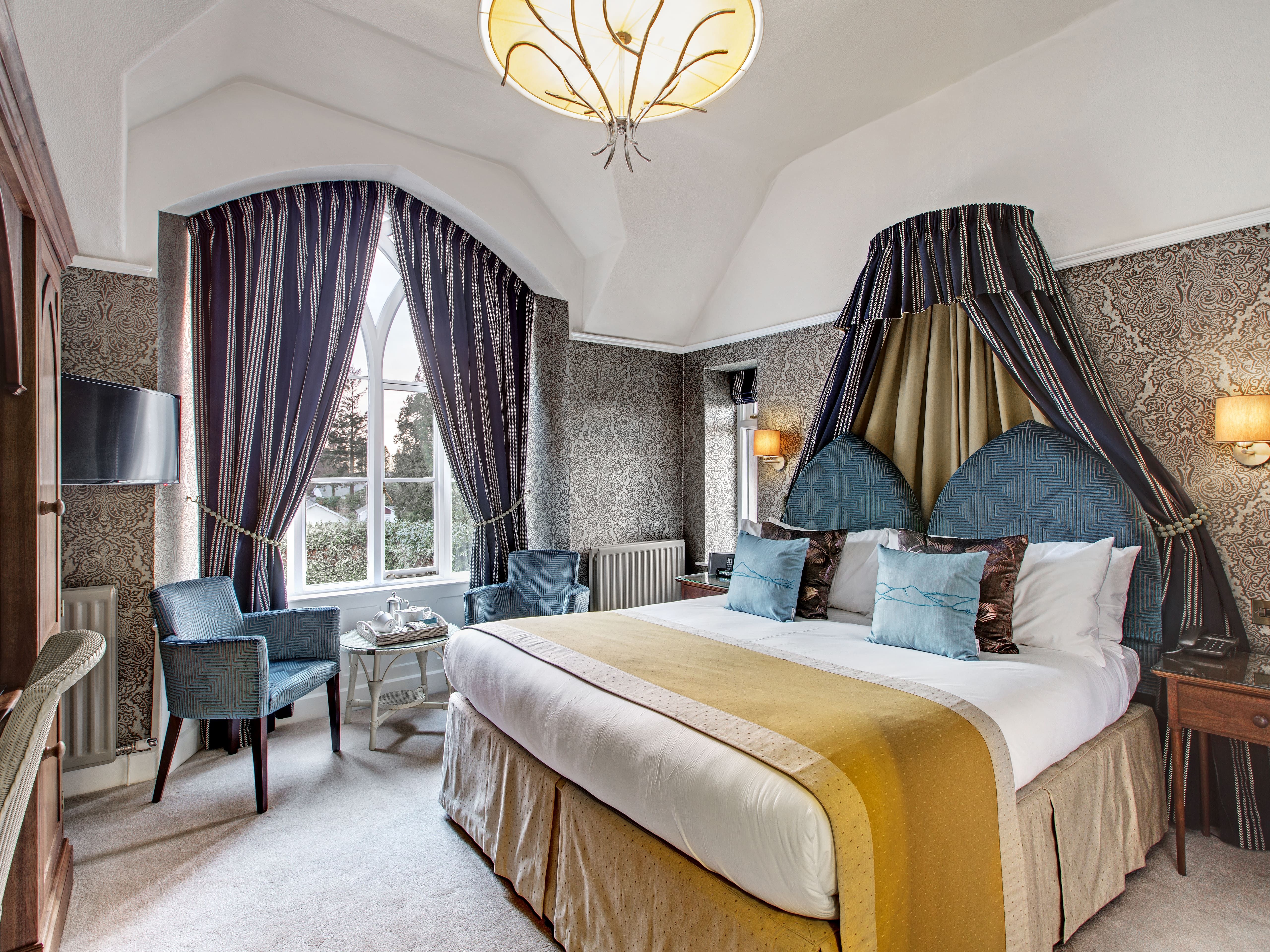 Elegant hotel bedroom with large bed, ornate curtains, and stylish seating area.