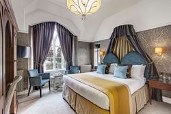 Elegant hotel bedroom with large bed, ornate curtains, and stylish seating area.