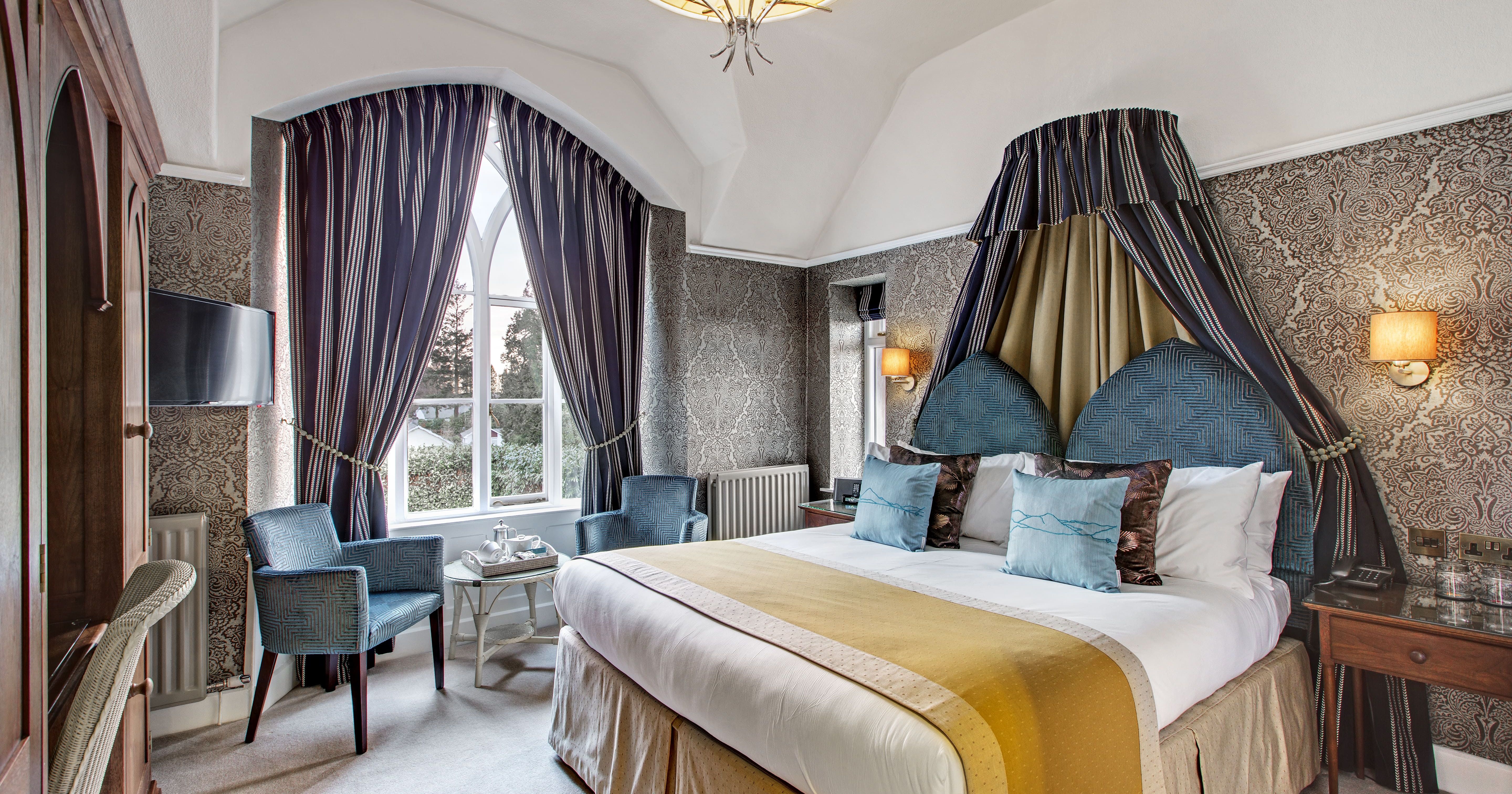 Elegant hotel bedroom with large bed, ornate curtains, and stylish seating area.