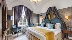 Elegant hotel bedroom with large bed, ornate curtains, and stylish seating area.