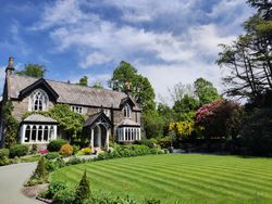 Charming stone house with arched windows surrounded by lush green garden and manicured lawn under a blue sky.