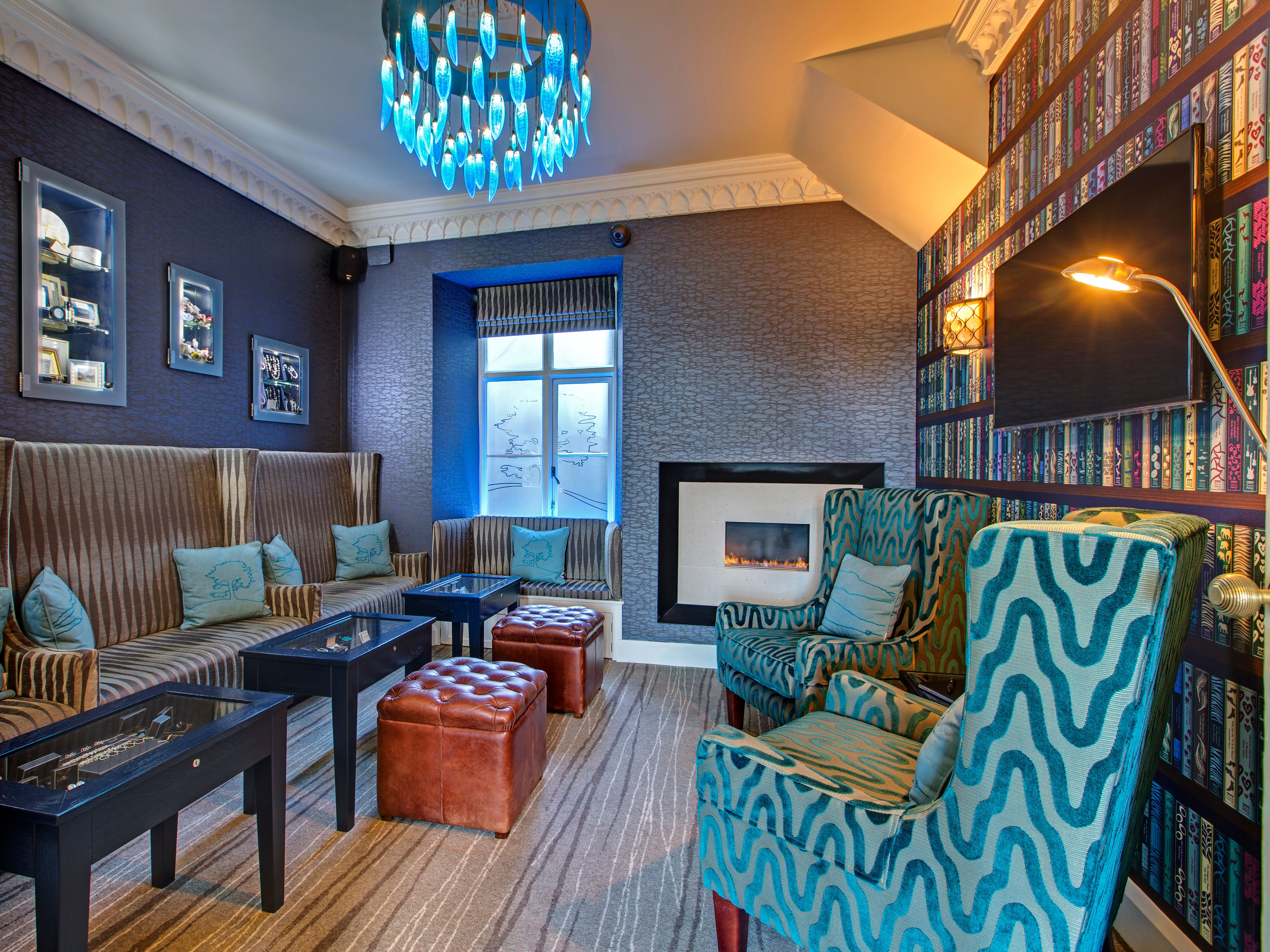 Colorful and cozy lounge with patterned chairs, modern fireplace, and blue chandelier