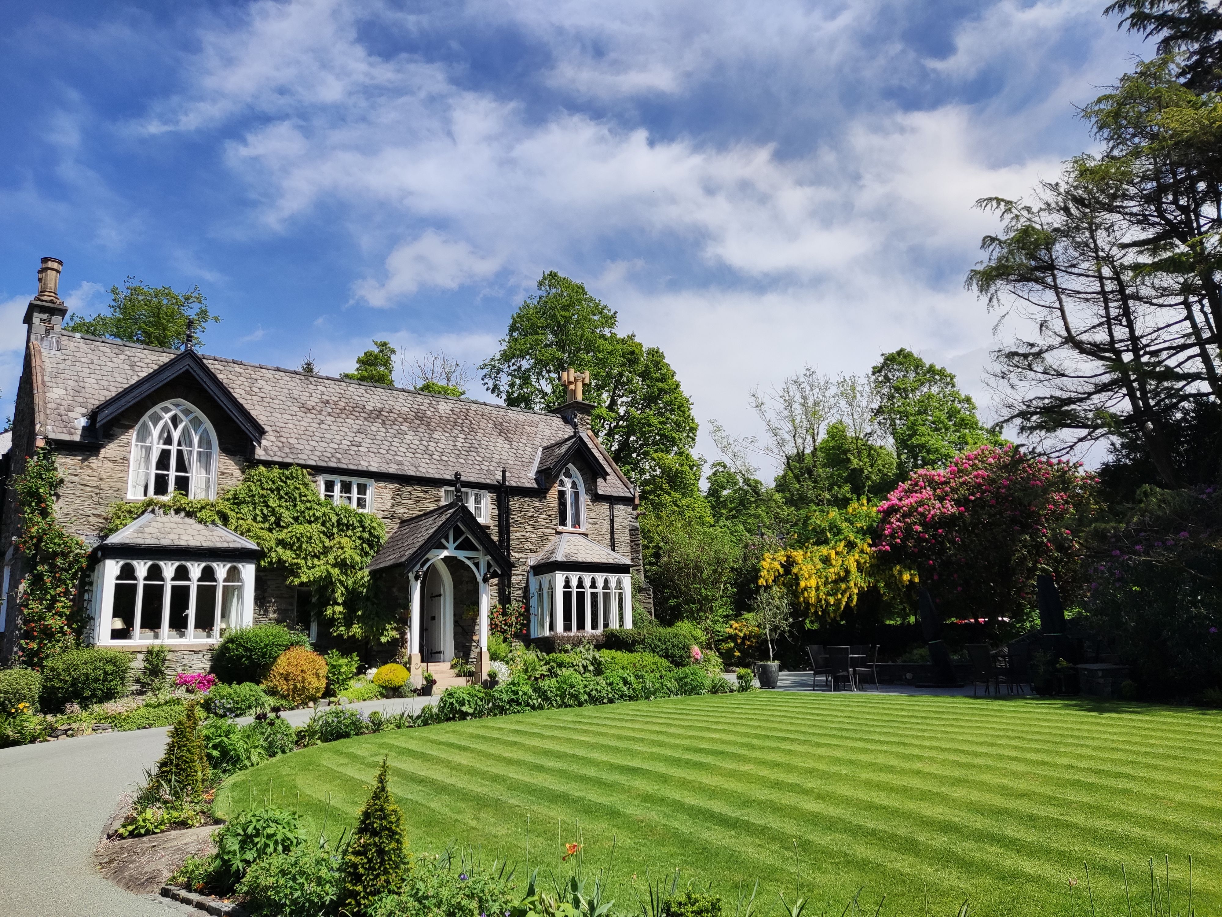 Stone house with arched windows and a well-manicured lawn surrounded by vibrant gardens