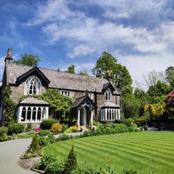 Stone house with arched windows and a well-manicured lawn surrounded by vibrant gardens