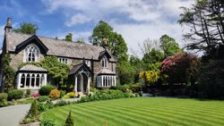 Stone house with arched windows and a well-manicured lawn surrounded by vibrant gardens