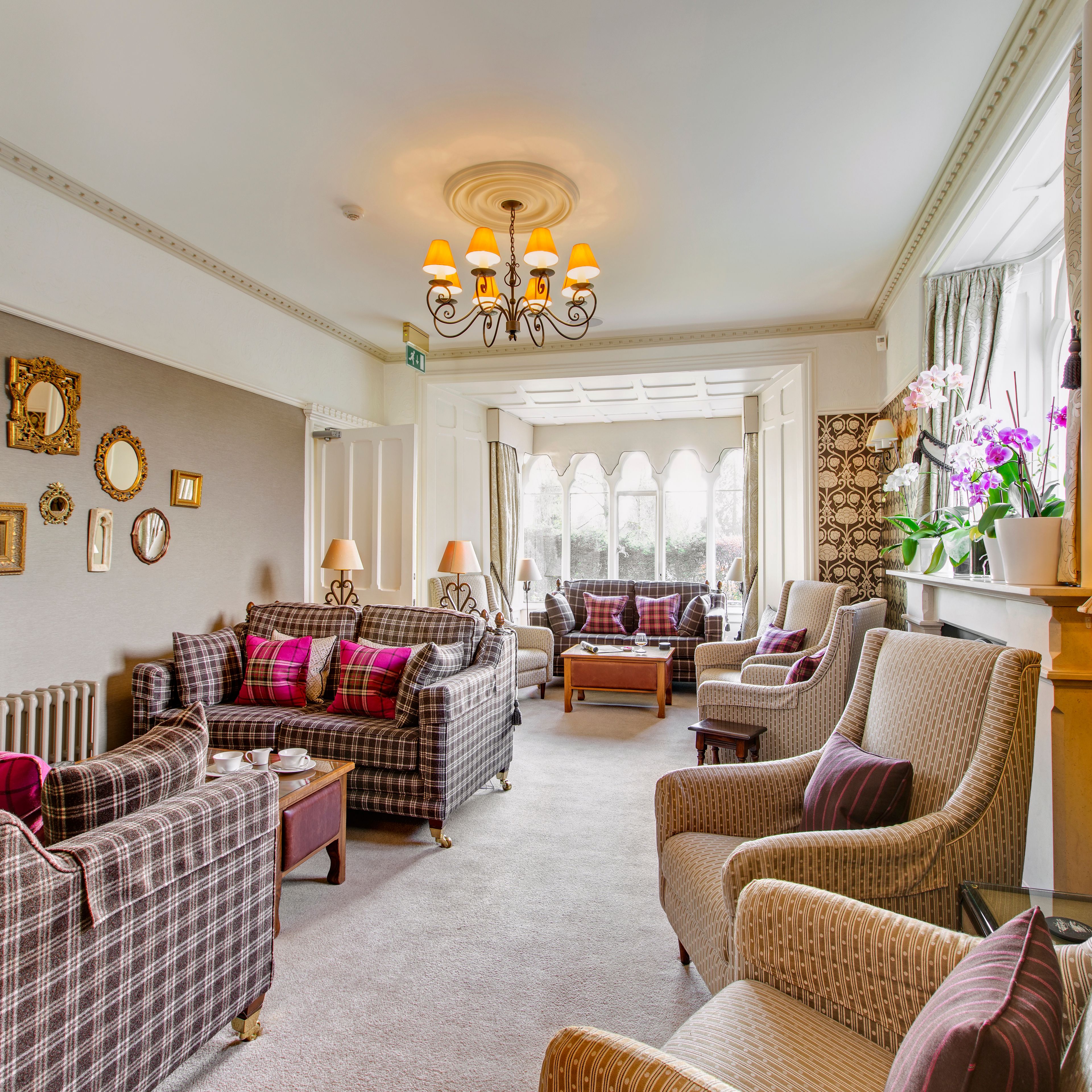 Elegant lounge with patterned sofas, armchairs, decorative mirrors, and large windows
