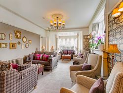 Elegant lounge with patterned sofas, armchairs, decorative mirrors, and large windows