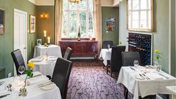 Elegant restaurant dining room with white tablecloths, wine rack, and large window.