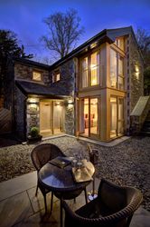 Modern stone house with large windows and patio seating at dusk