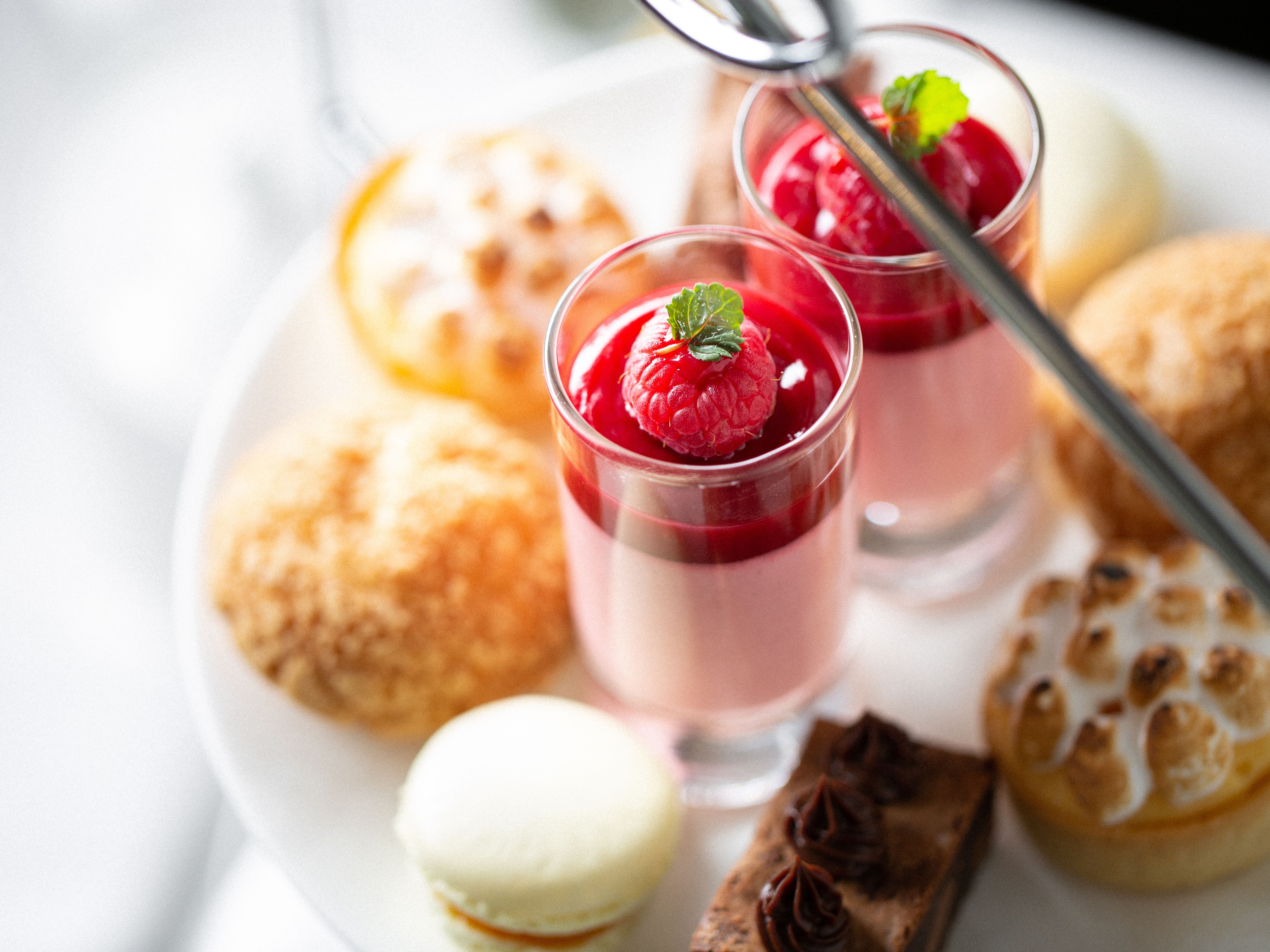 Assorted desserts on a white plate, including raspberry panna cotta served in glasses, macarons, tartlets, and pastries.