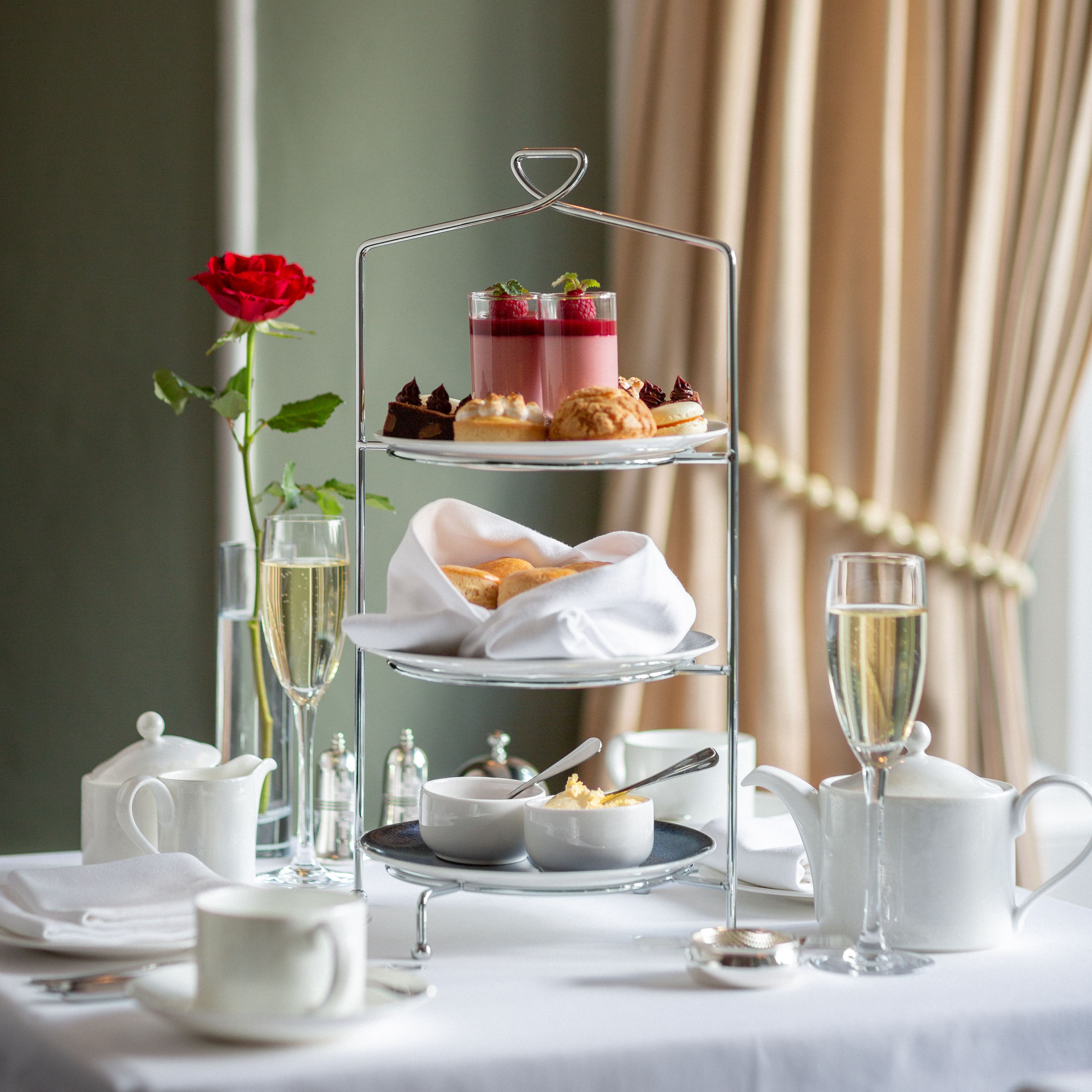 Elegant afternoon tea set with pastries, scones, and champagne on a white tablecloth.