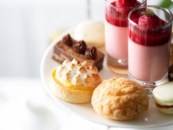 Assorted French pastries and desserts on a white platter including tart, choux pastry, macaron, brownie, and raspberry mousse.